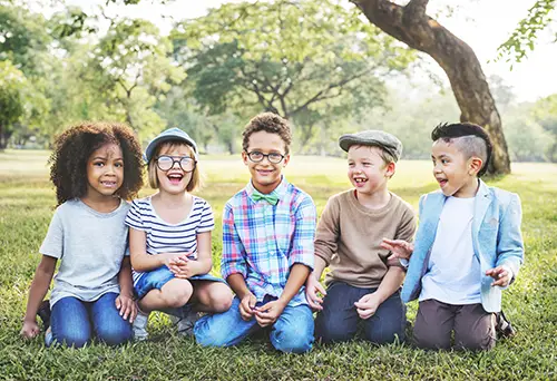 Five smiling kids sitting outside.